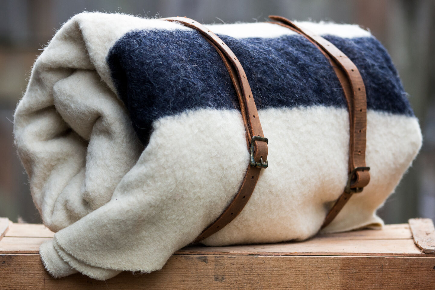 A close-up of a white blanket with a dark blue stripe rolled up and held together with brown leather straps. A close-up of a white blanket with a dark blue stripe rolled up and held together with brown leather straps.