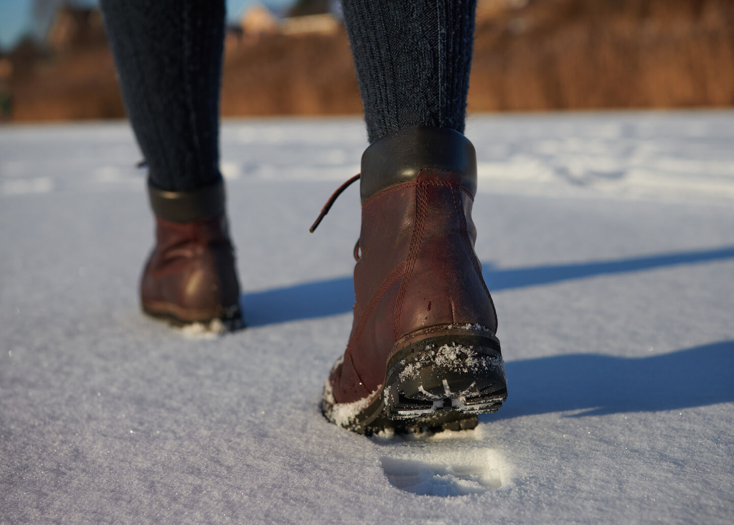 A close-up of a woman's legs walking in the snow while wearing brown leather boots during the winter season.