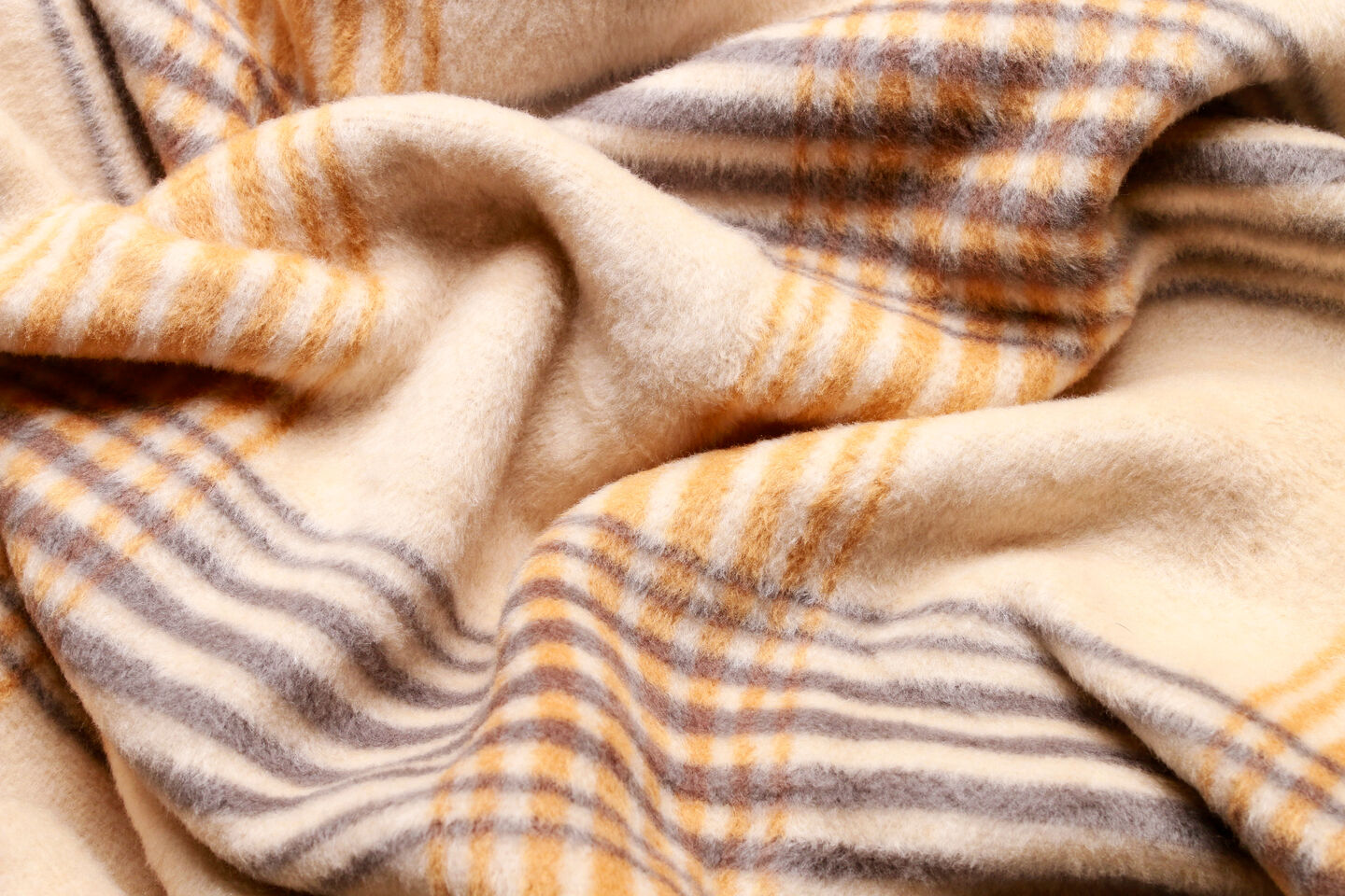 A plaid-patterned wool blanket draped over a fluffy white bed, exuding warmth and inviting comfort in a softly lit room.